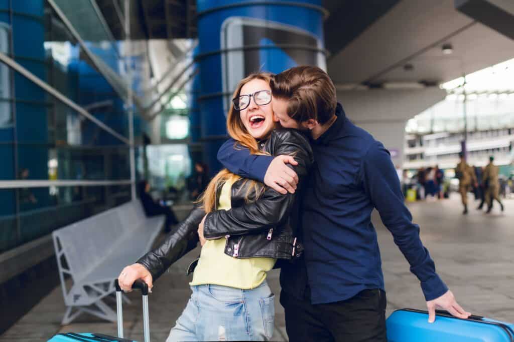 portrait-handsome-guy-with-beard-black-shirt-kissing-girl-with-long-hair-outside-airport-she-wears-glasses-yellow-sweater-jacket-with-jeans-she-looks-happy 情侶出國