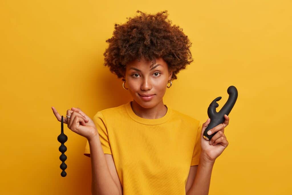 pretty-young-woman-gets-sexual-experience-with-sex-toy-accessories-holds-anal-beads-stimulate-erogenous-zone-your-anus-vibrator-reach-orgasm-stands-against-vivid-yellow-wall 後庭拉珠