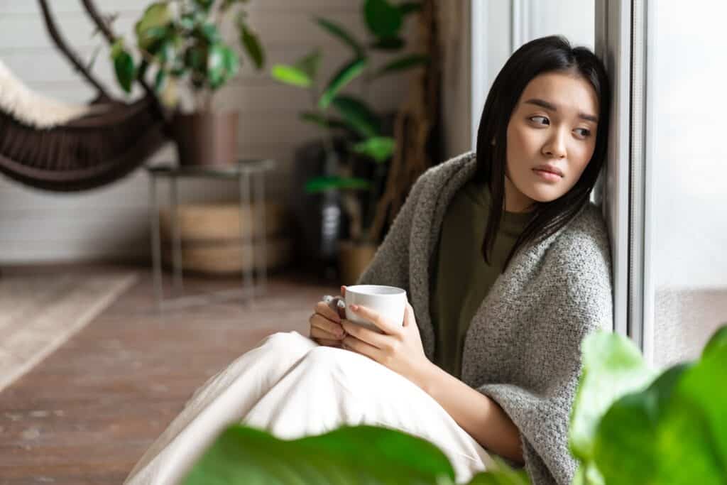 sad-asian-woman-looking-outside-window-sitting-floor-with-miserable-upset-face-drinking-coffee 寂寞